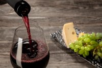 A bottle and a glass of red wine with fruits over wooden background © Freepik